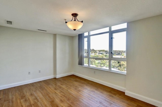 spare room with light wood-type flooring, visible vents, and baseboards