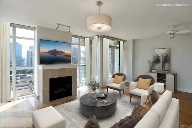 living area featuring a ceiling fan, expansive windows, track lighting, a tile fireplace, and baseboards