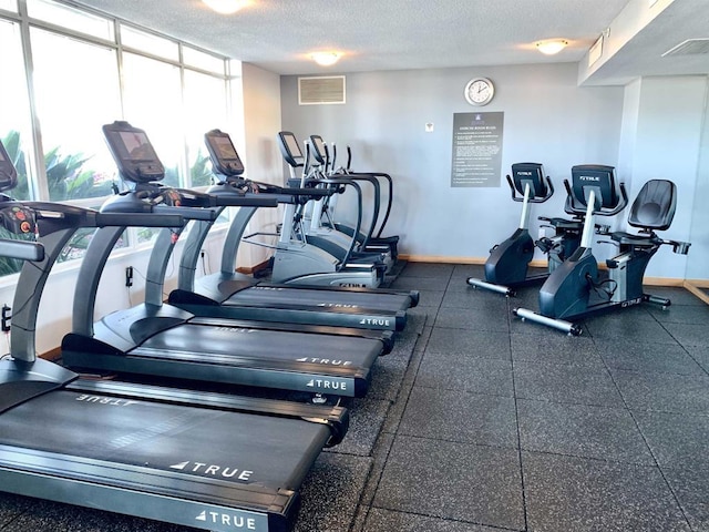 gym with baseboards, expansive windows, visible vents, and a textured ceiling