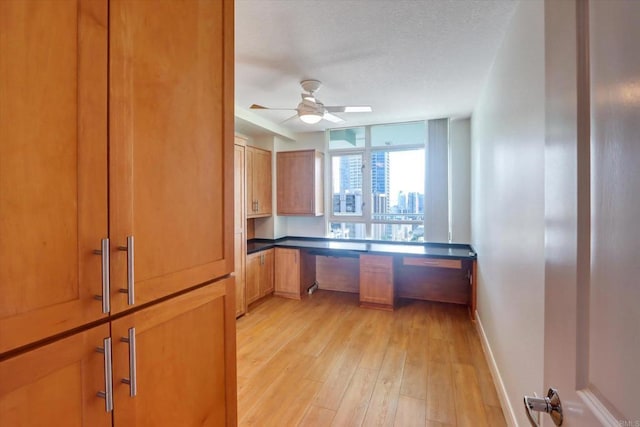 kitchen featuring ceiling fan, baseboards, light wood finished floors, dark countertops, and built in desk