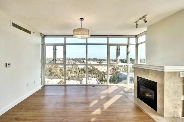 unfurnished living room featuring a fireplace, visible vents, a wall of windows, and wood finished floors