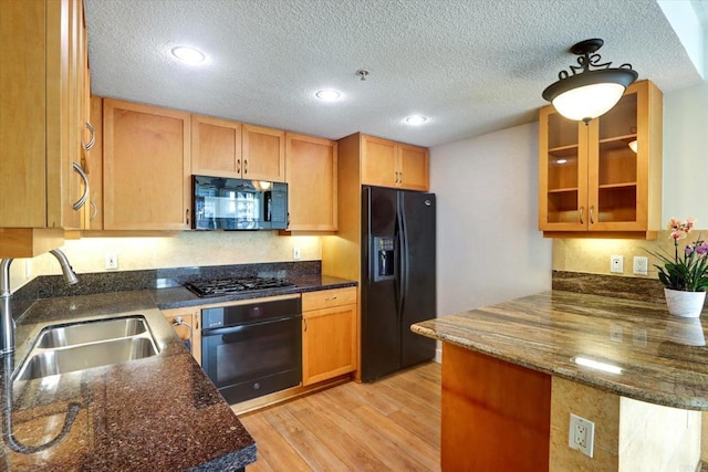 kitchen with a peninsula, a sink, light wood-style floors, black appliances, and dark stone countertops