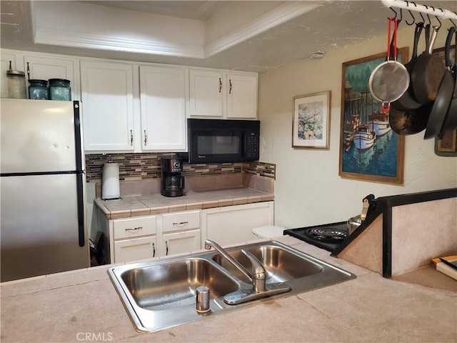 kitchen featuring tile counters, a sink, freestanding refrigerator, white cabinets, and black microwave
