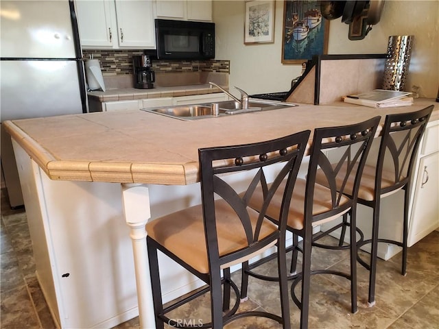 kitchen featuring decorative backsplash, tile countertops, a sink, black microwave, and freestanding refrigerator