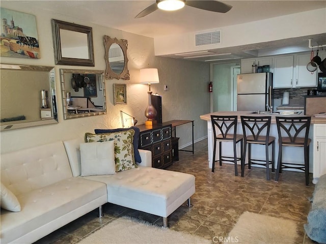 living room with a textured wall, visible vents, and a ceiling fan