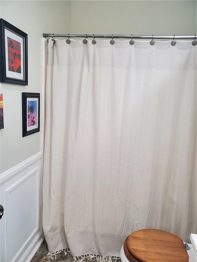 full bathroom with a decorative wall, toilet, and wainscoting