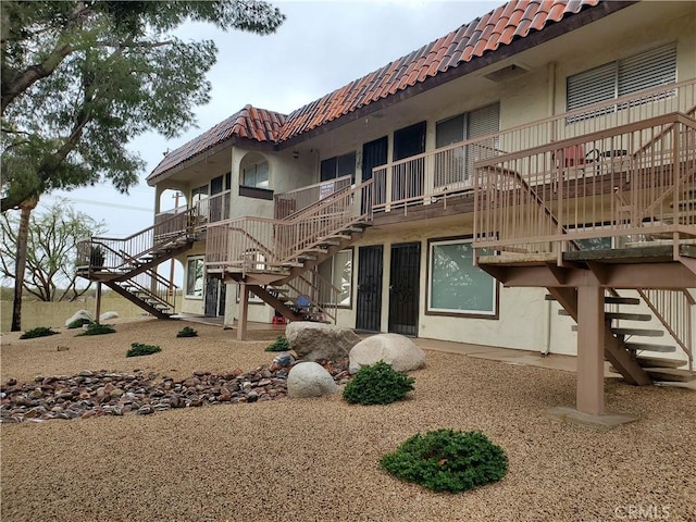 rear view of house featuring a tile roof, stairway, and stucco siding