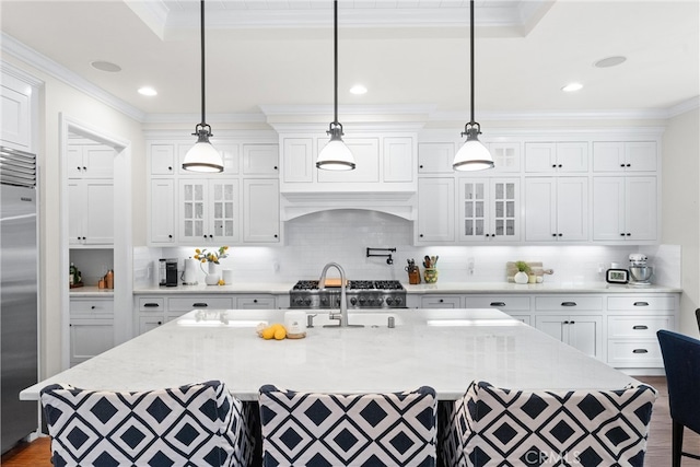 kitchen with an island with sink, ornamental molding, stainless steel built in refrigerator, and white cabinets