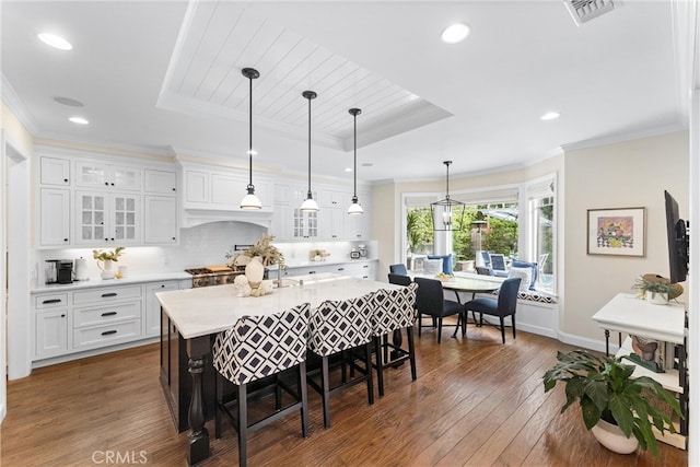 kitchen featuring dark wood-style floors, a raised ceiling, light countertops, ornamental molding, and white cabinets