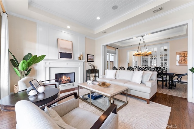 living area with an inviting chandelier, a fireplace, a tray ceiling, and dark wood finished floors