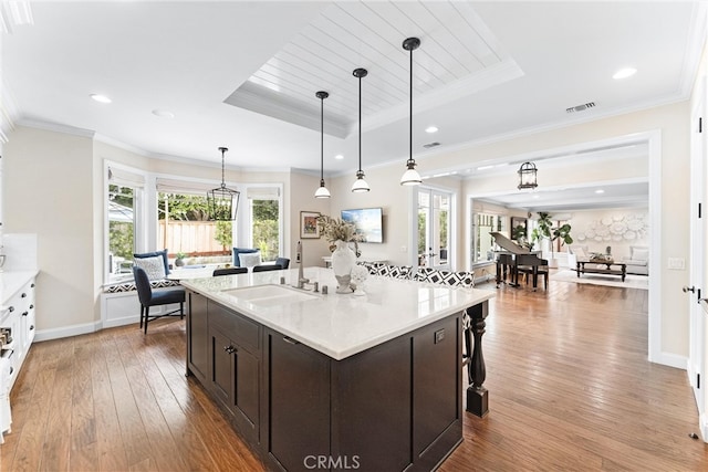 kitchen with crown molding, a raised ceiling, visible vents, wood-type flooring, and a sink