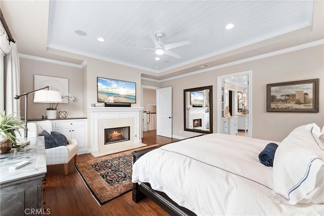 bedroom featuring a tray ceiling, crown molding, recessed lighting, wood-type flooring, and a lit fireplace