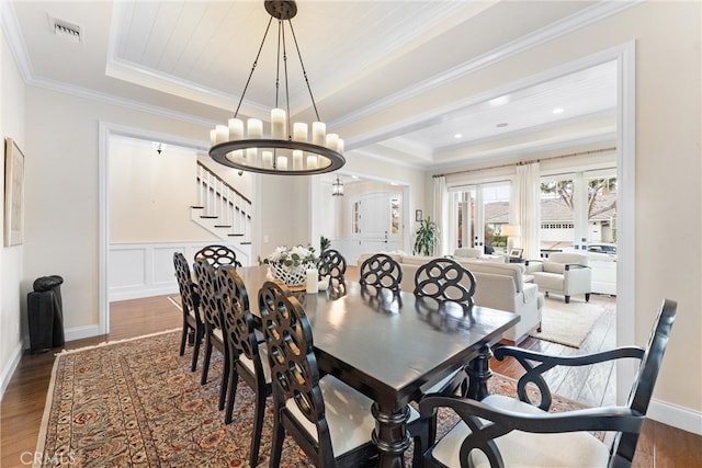 dining space with a tray ceiling, visible vents, stairway, ornamental molding, and wood finished floors