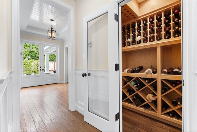 wine cellar with a decorative wall, ornamental molding, wainscoting, hardwood / wood-style floors, and a raised ceiling