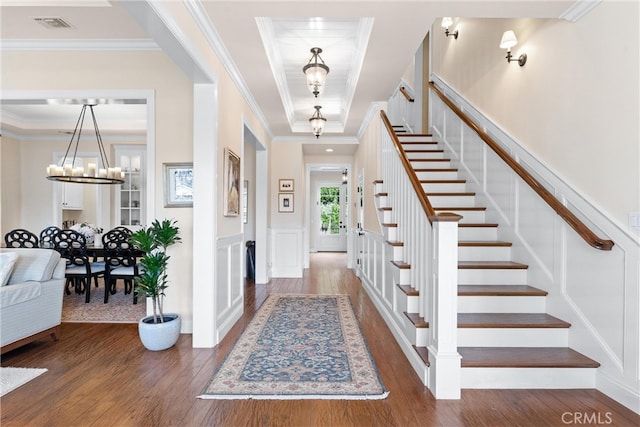 foyer entrance with crown molding, stairway, wood finished floors, and a decorative wall