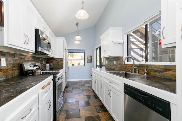 kitchen featuring decorative light fixtures, stainless steel appliances, dark countertops, white cabinets, and a sink