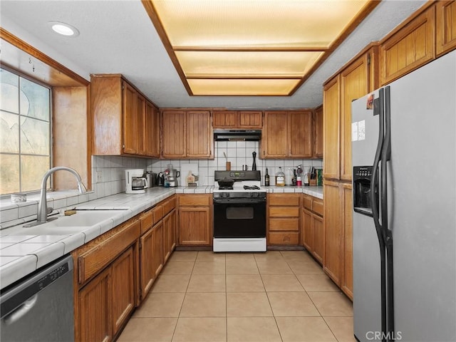 kitchen with tile countertops, appliances with stainless steel finishes, brown cabinetry, and a sink