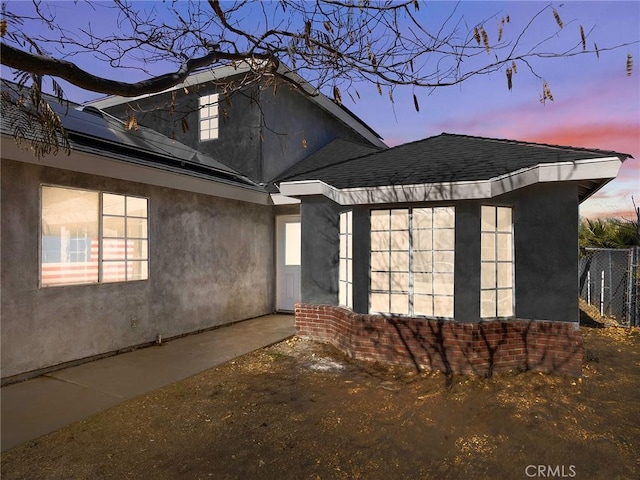 exterior space featuring stucco siding, brick siding, fence, and roof with shingles