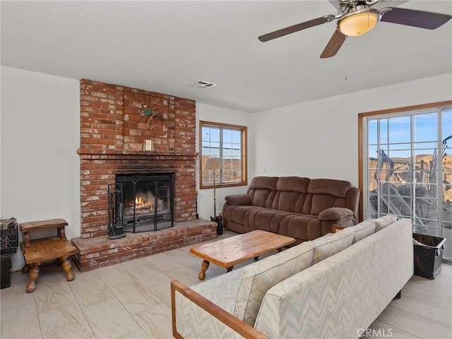 living area featuring a brick fireplace, visible vents, and a ceiling fan