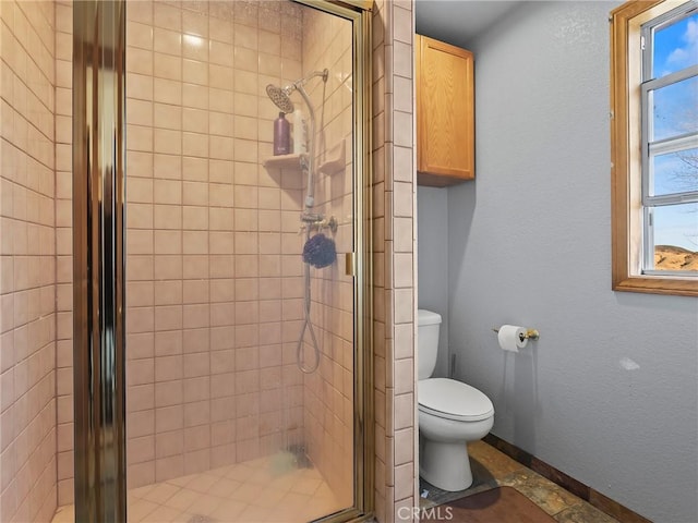 full bathroom with a textured wall, a stall shower, toilet, and baseboards