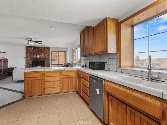 kitchen with a fireplace, tile countertops, stainless steel dishwasher, open floor plan, and a peninsula