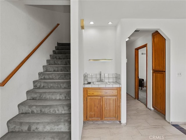 bar with arched walkways, a sink, stairs, indoor wet bar, and recessed lighting