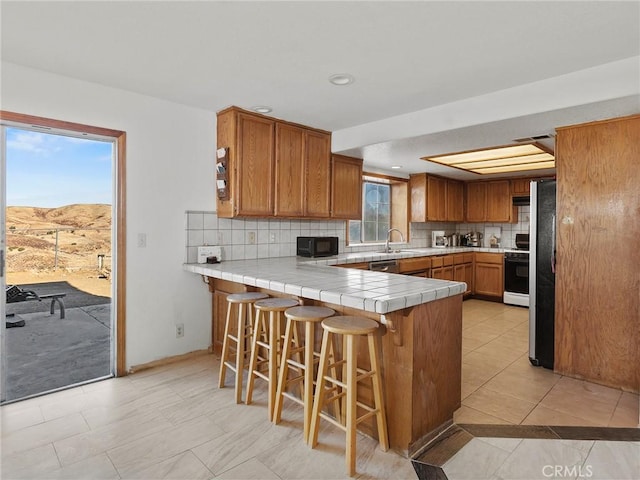 kitchen with tile countertops, a peninsula, a kitchen breakfast bar, and brown cabinets