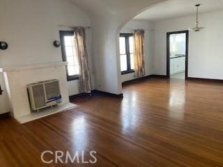 unfurnished living room with a fireplace, arched walkways, and dark wood-style flooring