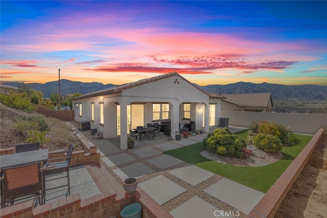 back of house at dusk featuring stucco siding, outdoor dining space, a patio area, a mountain view, and a fenced backyard