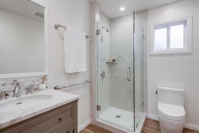 bathroom featuring toilet, wood finished floors, baseboards, tasteful backsplash, and a stall shower