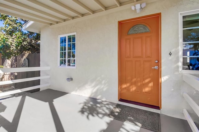 view of exterior entry featuring fence and stucco siding