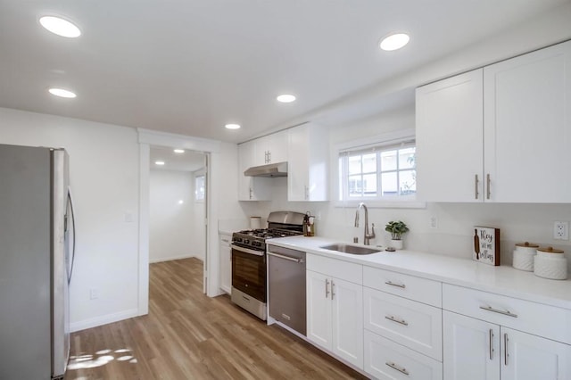 kitchen featuring under cabinet range hood, stainless steel appliances, a sink, white cabinetry, and light countertops