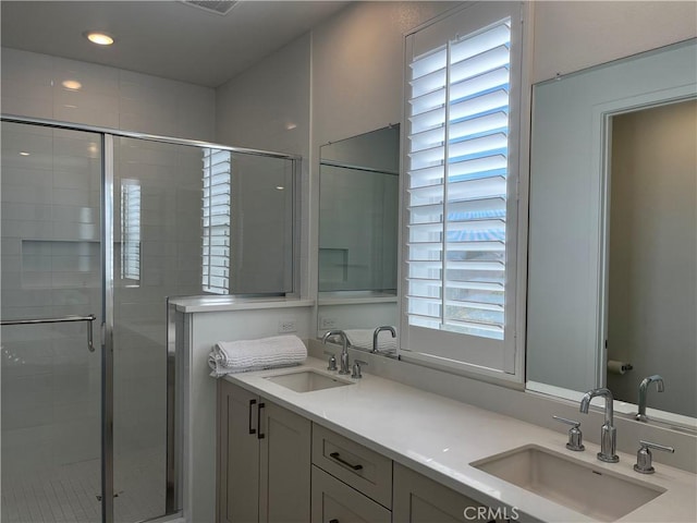 full bathroom with double vanity, a stall shower, a sink, and visible vents