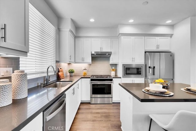 kitchen with white cabinets, dark countertops, stainless steel appliances, under cabinet range hood, and a sink