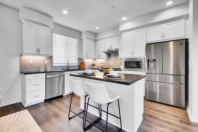 kitchen with dark countertops, under cabinet range hood, a kitchen island, and appliances with stainless steel finishes