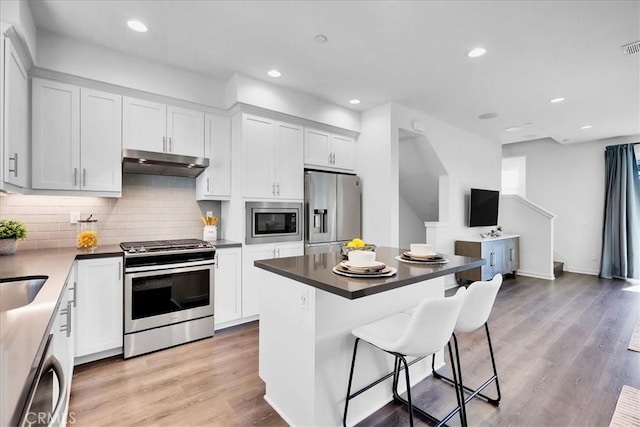 kitchen with a kitchen island, wood finished floors, stainless steel appliances, under cabinet range hood, and white cabinetry