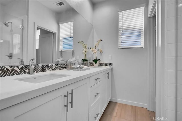 bathroom with a sink, visible vents, tile patterned floors, double vanity, and tasteful backsplash