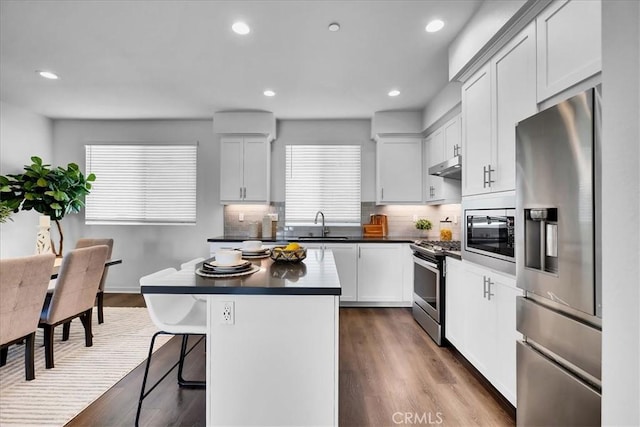 kitchen with dark countertops, appliances with stainless steel finishes, a center island, under cabinet range hood, and white cabinetry