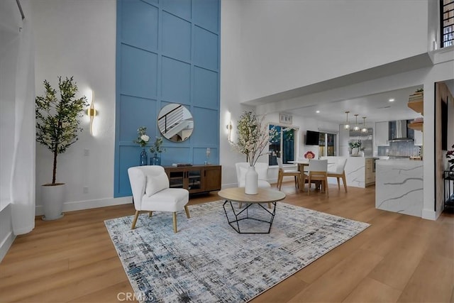 sitting room featuring light wood finished floors, a high ceiling, and baseboards