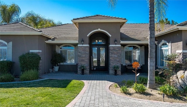 view of exterior entry with stone siding, a tile roof, a lawn, and stucco siding