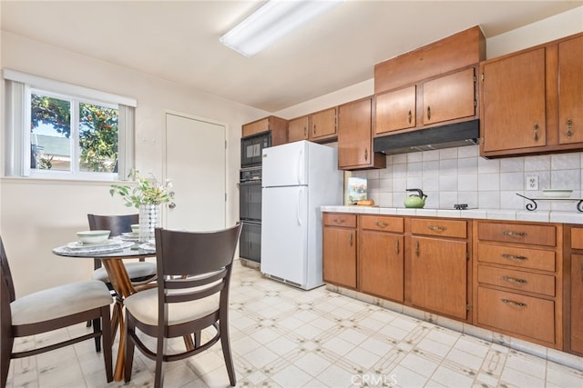 kitchen with black appliances, light floors, brown cabinets, and under cabinet range hood