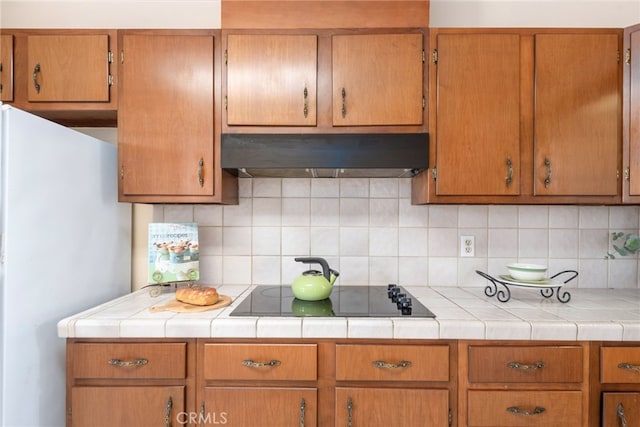 kitchen with black electric stovetop, ventilation hood, backsplash, and freestanding refrigerator