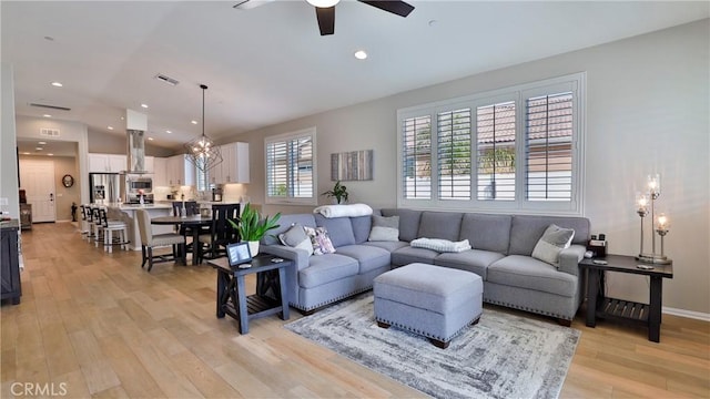 living room featuring ceiling fan with notable chandelier, light wood finished floors, visible vents, and recessed lighting