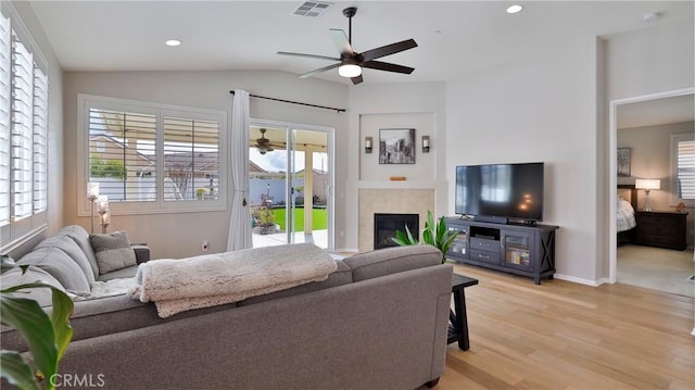 living area featuring lofted ceiling, light wood-type flooring, ceiling fan, and a tile fireplace