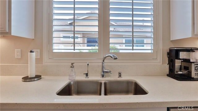 interior details with white cabinets, a sink, and light stone countertops