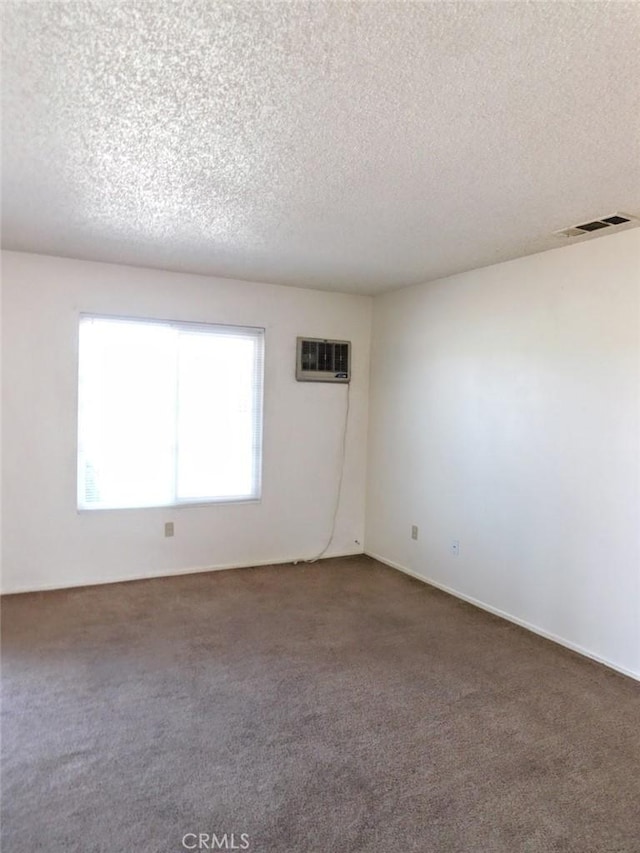 carpeted spare room with visible vents, a textured ceiling, and a wall mounted AC