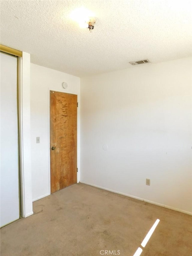 spare room with a textured ceiling, carpet flooring, and visible vents