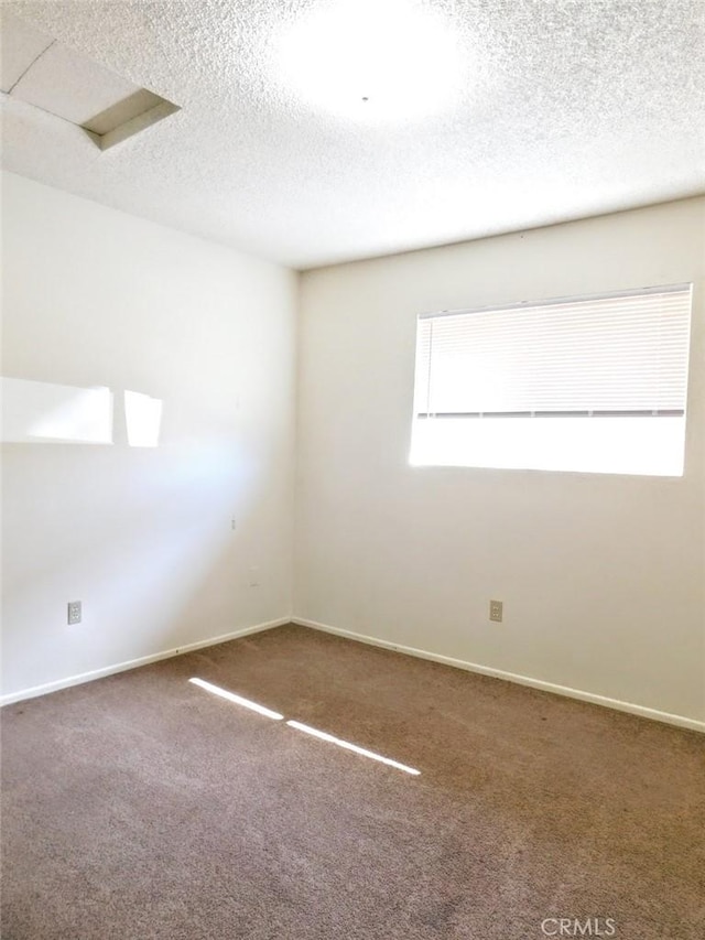 spare room with a textured ceiling, carpet floors, and baseboards