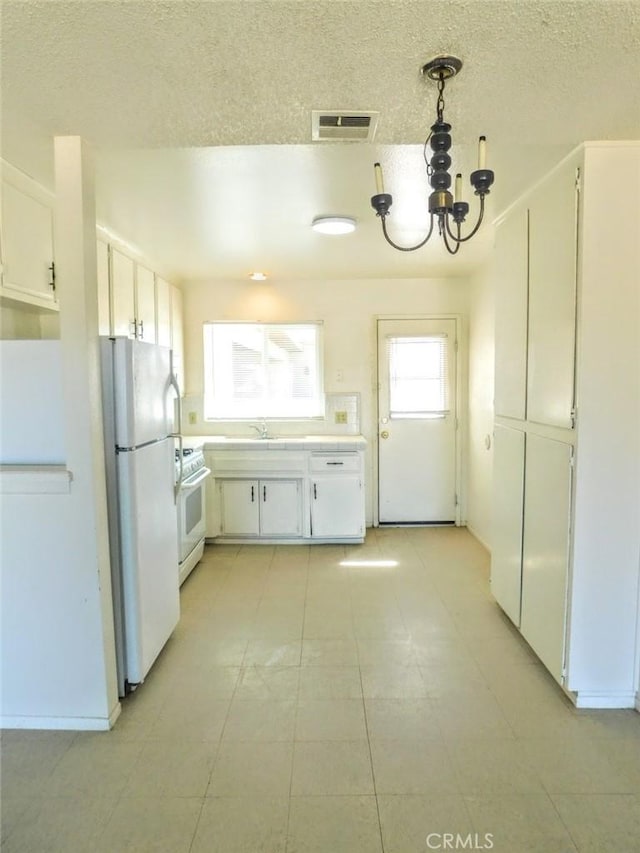 kitchen with white appliances, white cabinetry, hanging light fixtures, and visible vents