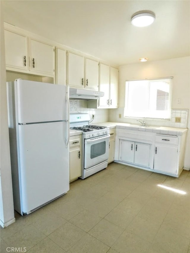 kitchen featuring white appliances, decorative backsplash, under cabinet range hood, white cabinetry, and a sink